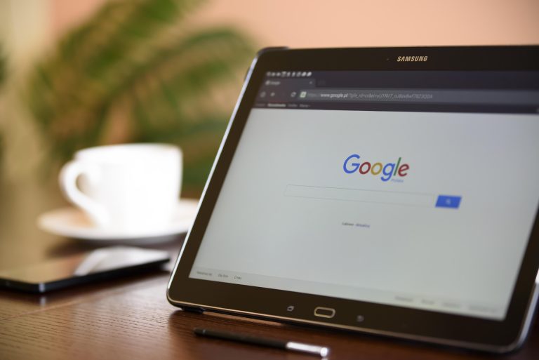 Tablet a w tle filiżanka kawy i telefon na stole.
